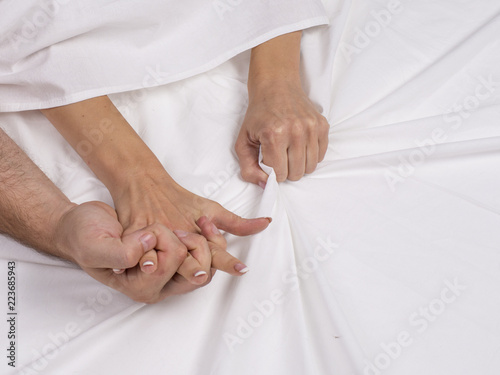 Close up of couple hands lie on bed in bedroom, lovers have intense sex or making love feeling orgasm and satisfaction, boyfriend and girlfriend enjoy foreplay on white sheets.