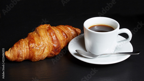  Cup of coffee with a croissant on a dark background.