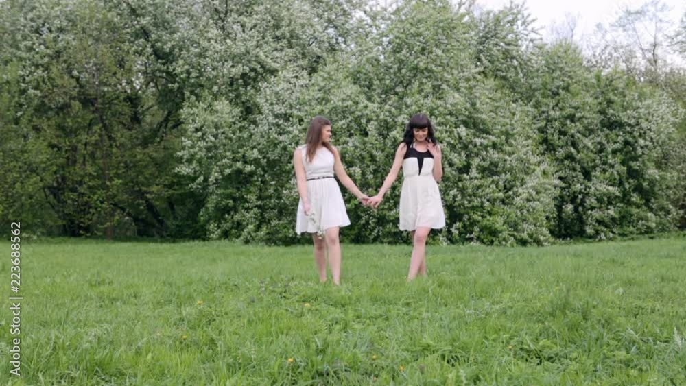 Couple young beautiful woman enjoying smell of blooming tree on a sunny day. Outdoor portrait in a blooming spring park Couple young beautiful woman enjoying smell of blooming tree on a sunny day. Outdoor portrait in a blooming spring park
