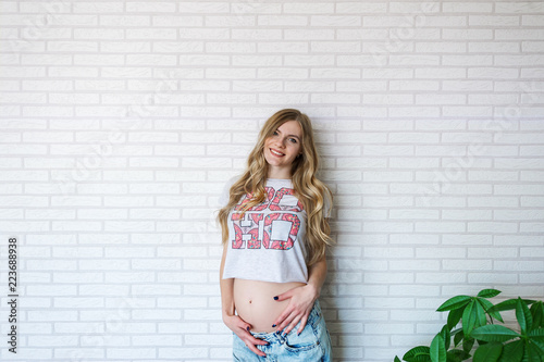 Young pregnant woman dressed in jeans on the brick wall background.
