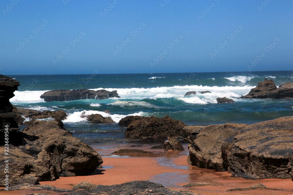 Portugal Ursa Beach at atlantic coast of Atlantic Ocean with rocks and foam at sand of coastline picturesque landscape panorama. Stones with green moss.