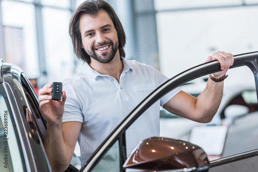 portrait of happy man with car key standing at new car in dealership salon portrait of happy man with car key standing at new car in dealership salon