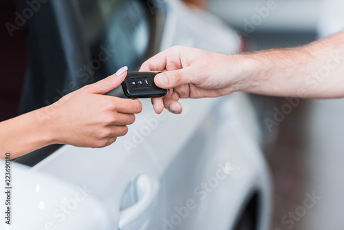 cropped shot of man giving car key to woman at dealership salon