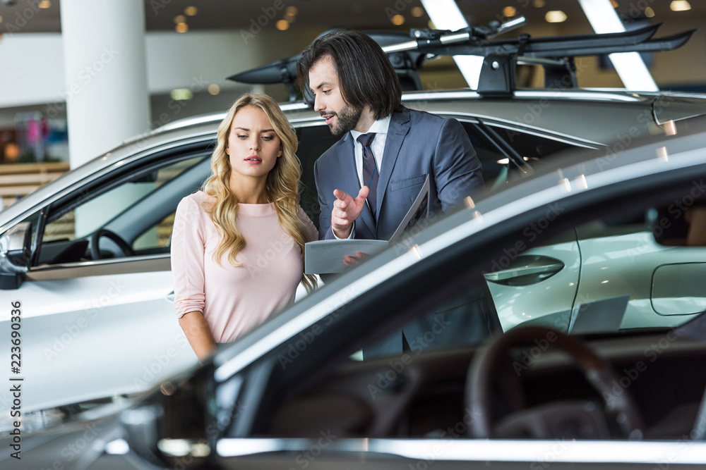 seller in formal wear recommending automobile to woman at dealership salon seller in formal wear recommending automobile to woman at dealership salon
