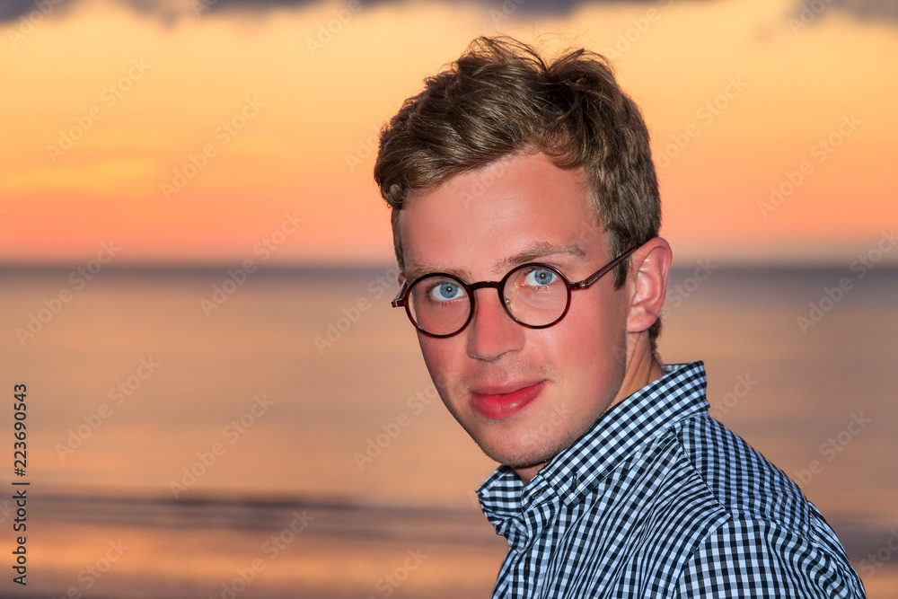 Fototapeta premium Beautiful portrait of a young caucasian man at sunset at the beach looking at the camera