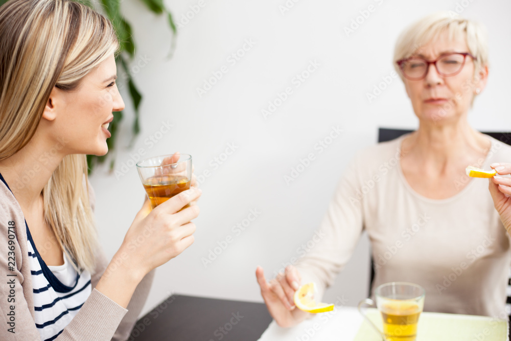 Senior mother and daughter talking and drinking tea in brightly lit dining room. Happy family moments at home Senior mother and daughter talking and drinking tea in brightly lit dining room. Happy family moments at home
