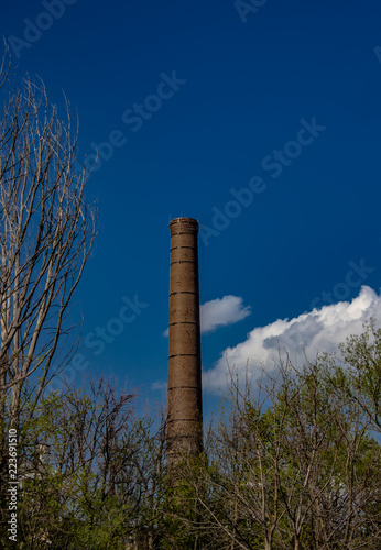 Obraz na płótnie A retired smokestack in the distance against a blue sky with white clouds. w salonie