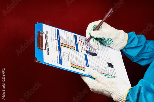 mechanic writes in the vehicle inspection report form on a red velvet background