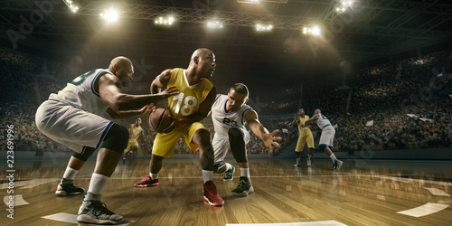 Basketball players on big professional arena during the game. Tense moment of the game. Male caucasian and black players fight for the ball © Alex