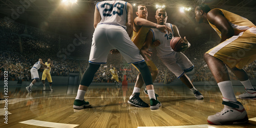 Basketball players on big professional arena during the game. Tense moment of the game. Male caucasian and black players fight for the ball © Alex
