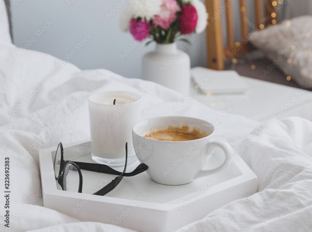 Coffee, candle and glasses on the tray standing on the bed.