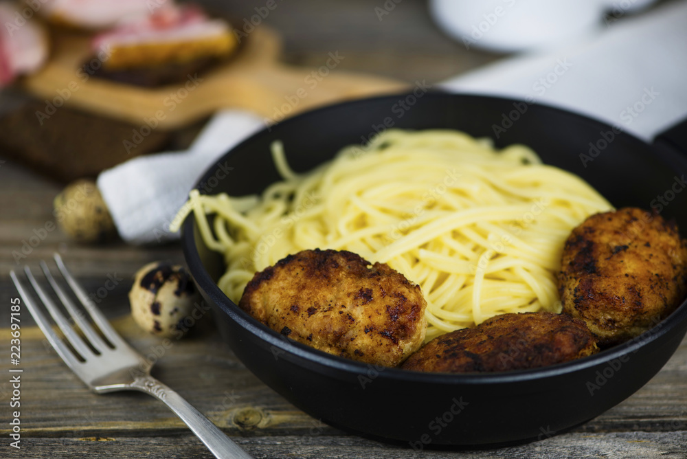 Spaghetti with meat cutlets in a frying pan on a wooden board Spaghetti with meat cutlets in a frying pan on a wooden board
