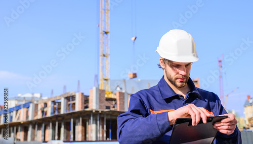 Engineer protective helmet stand in front of blue sky background. Contractor control according to plan. Builder engineer helmet works at construction site. Foreman control construction process
