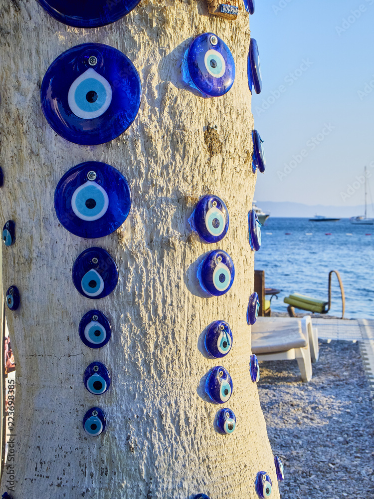 A lot of Nazar boncugu, a Turkish eye-shaped amulet screwed to a tree with  the Aegean Sea in the background. Stock Photo | Adobe Stock