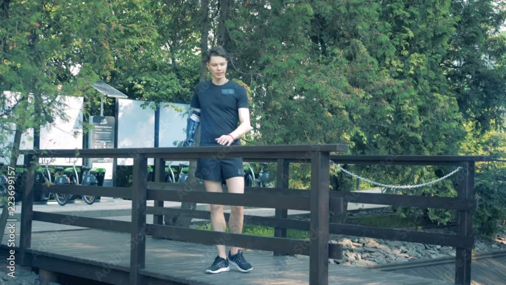 Male teenager with a prosthetic arm is walking along the bridge Male teenager with a prosthetic arm is walking along the bridge