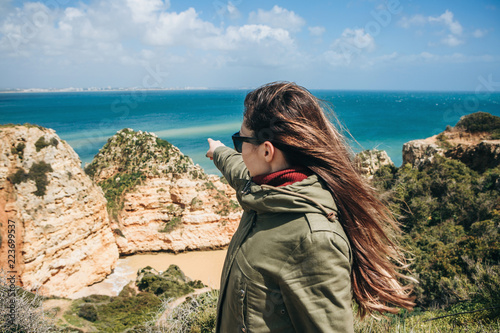 A tourist girl is pointing a hand at the beautiful view of the Atlantic Ocean off the coast of Portugal.