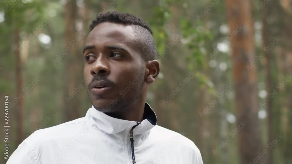 Tracking shot of confident black man standing in forest and looking away, then turning towards camera and smiling Tracking shot of confident black man standing in forest and looking away, then turning towards camera and smiling