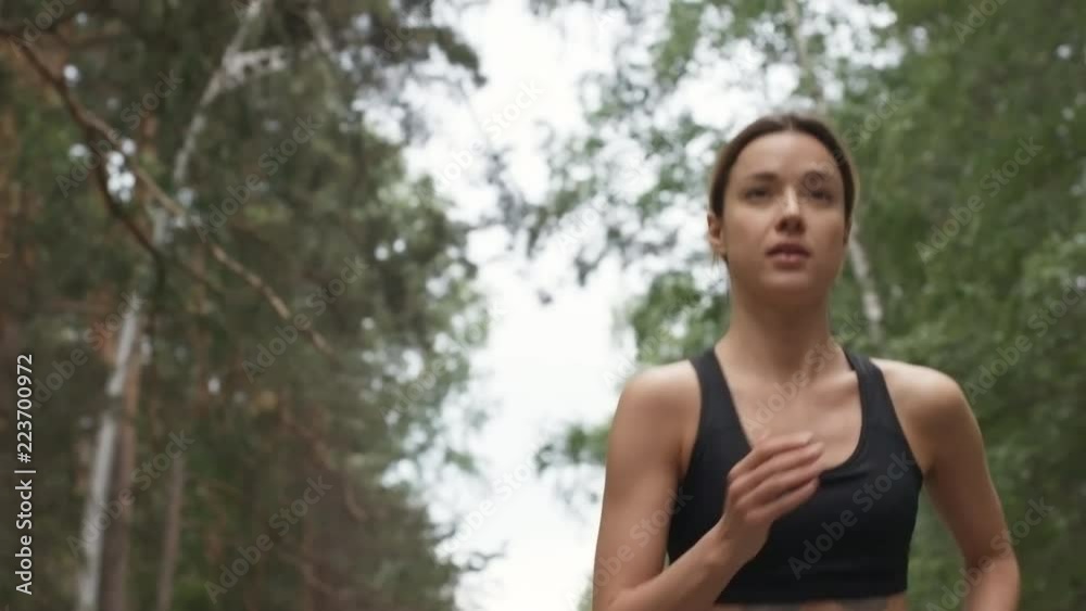 Dolly shot with tilt down of determined young sportswoman with fit body running along forest road in morning Dolly shot with tilt down of determined young sportswoman with fit body running along forest road in morning