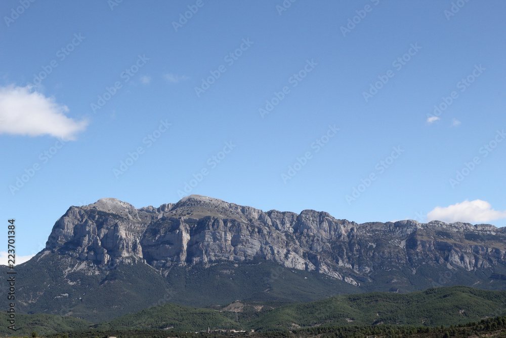 A landscape with blue sky, some clouds and the The Peña Montañesa mountain massif in the Spanish Aragonese Pyrenees, as seen from Ainsa, a small, stone made, rural town