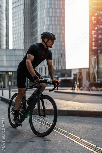 Cyclist riding professional bike next to modern buildings and skyscrapers.