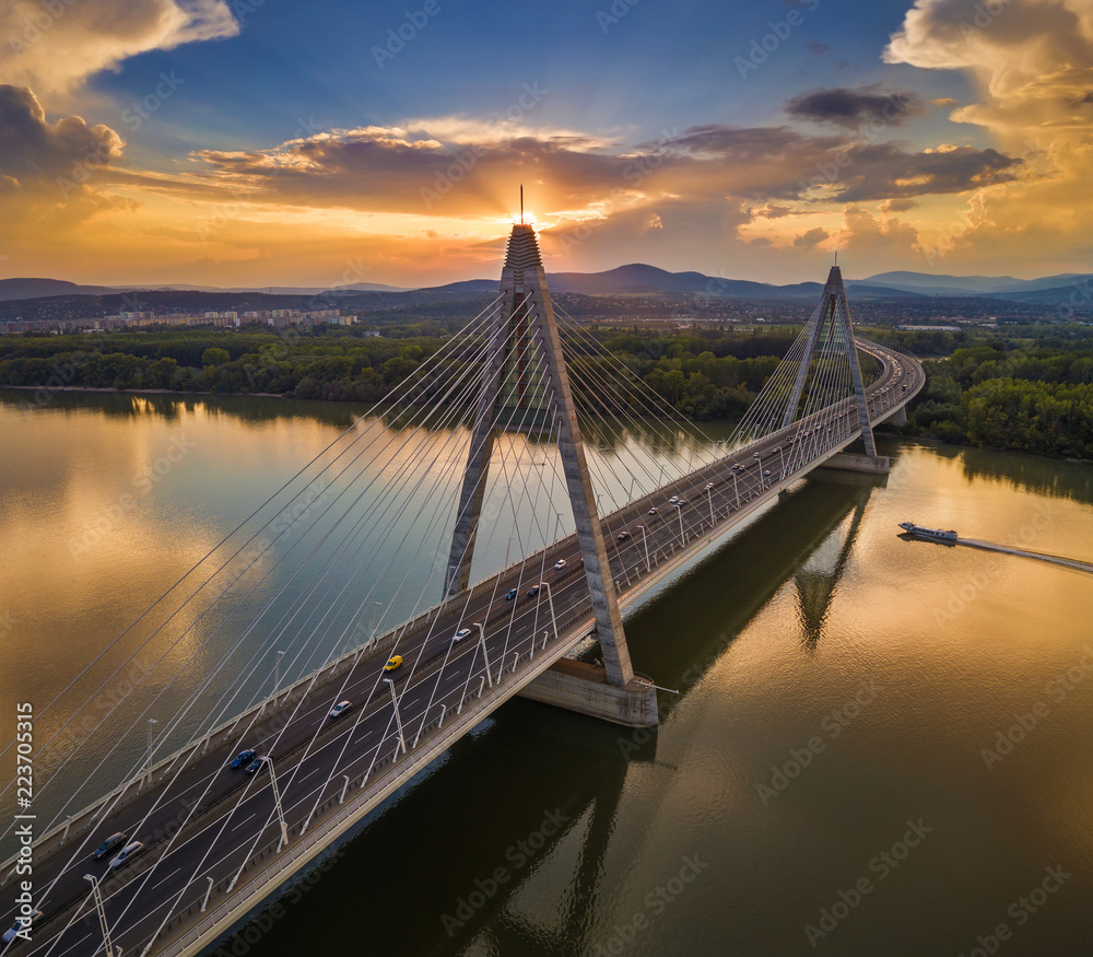 Obraz premium Budapest, Hungary - Megyeri Bridge at sunset with speedboat on River Danube and heavy traffic and beautiful blue & orange sky