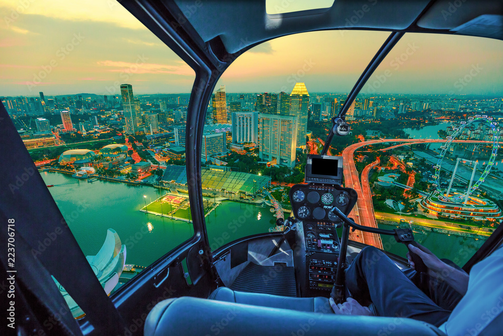 Fototapeta premium Malowniczy lot helikopterem nad panoramą zmierzchu Singapuru o świcie. Nocna scena z lotu ptaka z wnętrza kokpitu z panoramą Singapuru z diabelskim młynem o zachodzie słońca