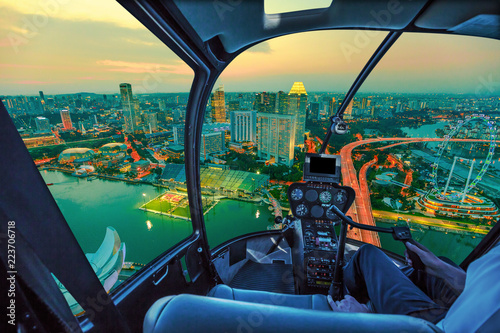 Scenic helicopter flight above Singapore twilight panorama at dawn. Night urban aerial scene from the cockpit interior with Singapore cityscape with ferris wheel at sunset.