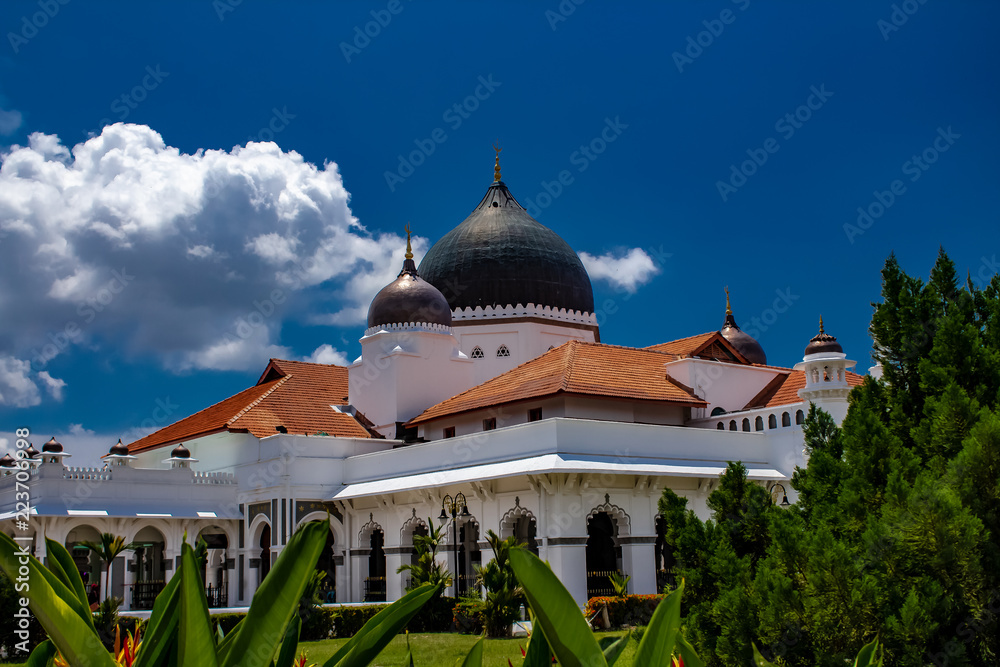 A white mosque with dark dome roof caps and a tile rooftop in Malaysaia
