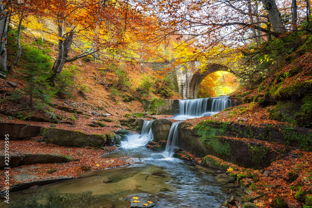 Fototapeta premium Jesień bajki przez rzekę / jesień rzeki z pięknymi kaskadami wody i stary most w pobliżu miejscowości Sitovo, Bułgaria
