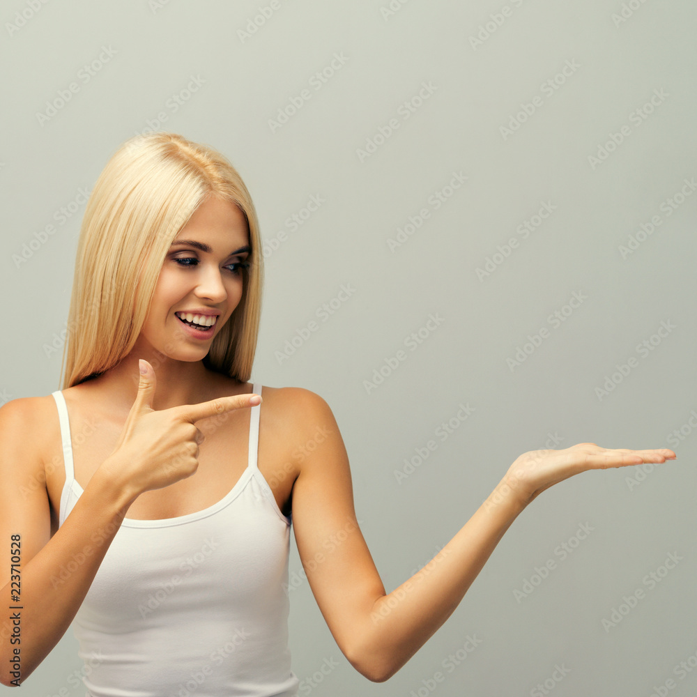 Fototapeta premium Woman in fitness wear, giving or showing something, or copyspace area for text, slogan, advertising, against grey.
