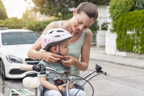 Mother and daughter, daughter wearing helmet sitting in children's seat