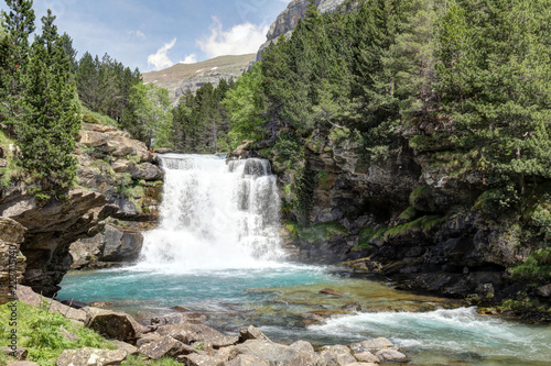 A rural landscape with Araza River waterfalls in the the pines and firs forest, with the Monte Perdido mountains on the background, in the Ordesa protected natural park in Aragon, Spain