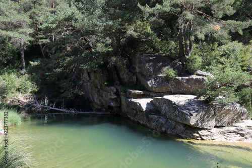 A small pond surrounded by firs and pines on big rock boulders on the Arba river, next to Luesia, a small tipical town located in Aragon, Spain