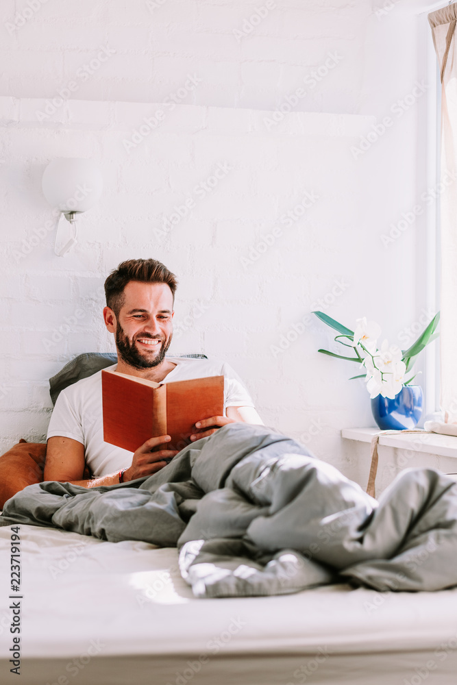 Fototapeta premium Young man reading a book in the bed