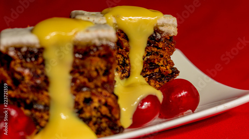 Fruitcake with pouring custard on red background