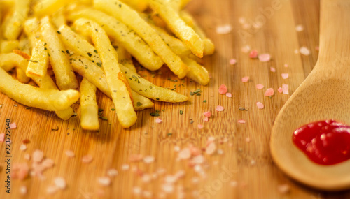 Potato fries plated on wooden board with ketchup (selective focus on fries)