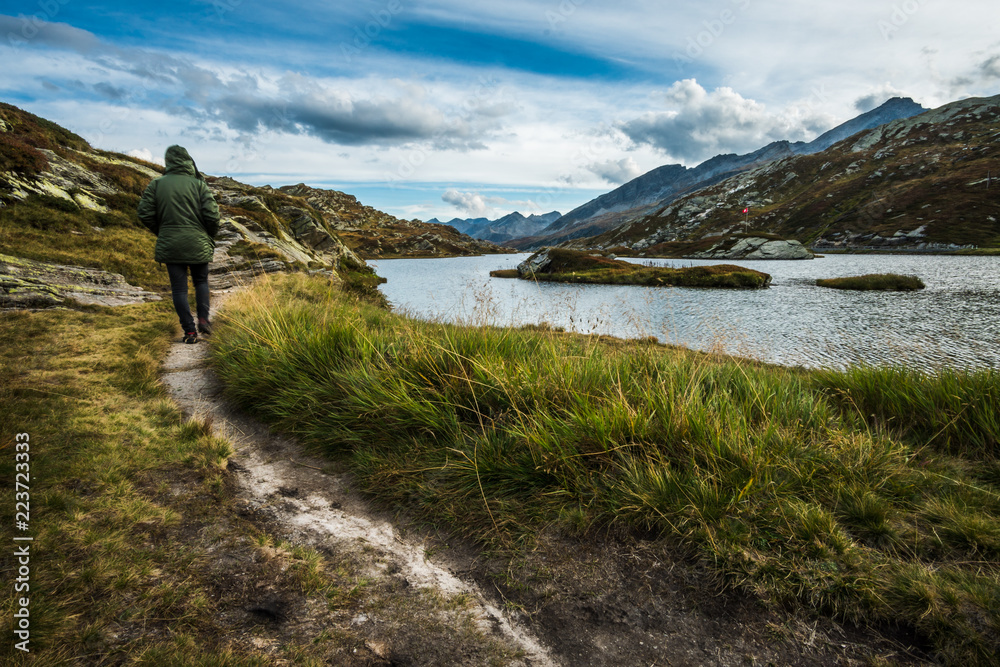 lonely trekking man walking in a mountains trail in switzerland alps with lake and cloudy sky lonely trekking man walking in a mountains trail in switzerland alps with lake and cloudy sky