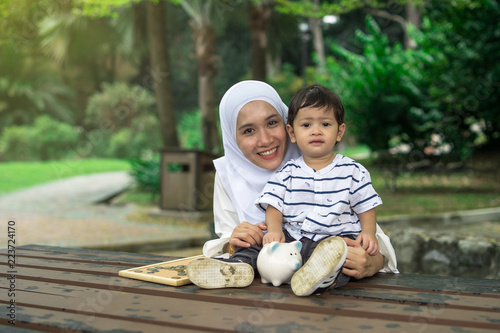 asian mother with her son at park with a piggy bank