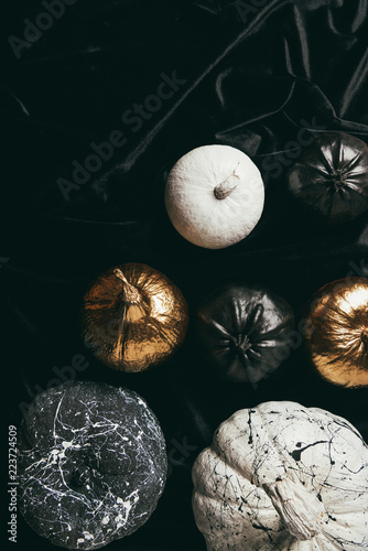 top view of festive decorative golden, black and white painted pumpkins on black cloth for halloween party photo