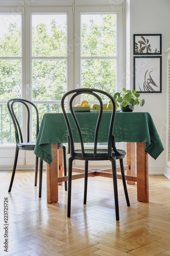Black chair next to a table with green cloth in a dining room interior. Balcony window in the background. Real photo