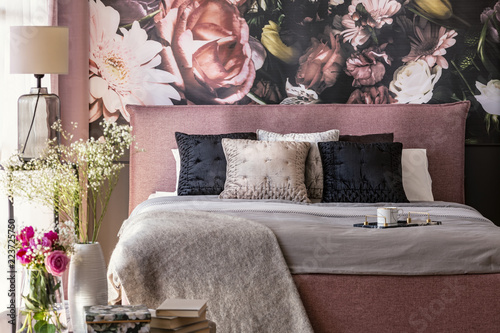 Pink and grey bed with cushions in patterned bedroom interior with flowers and lamp. Real photo photo