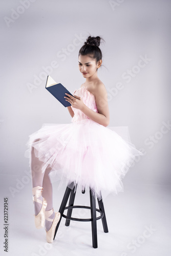 Beauty lady is wearing pink ballet dress and pink satin ballet shoes,sitting on black chair and read book,