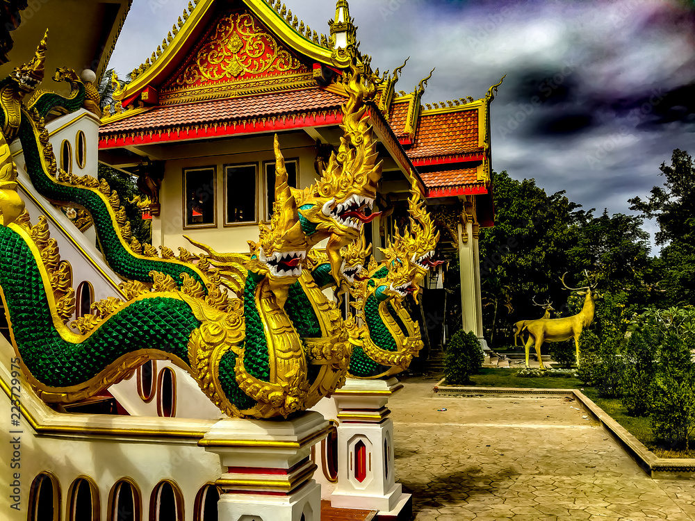 A bright gold and green carving of the multi-headed serpant god Naga n a white staircase appearing to slither down the railing. Wat That Phoun, Vientiane Laos.