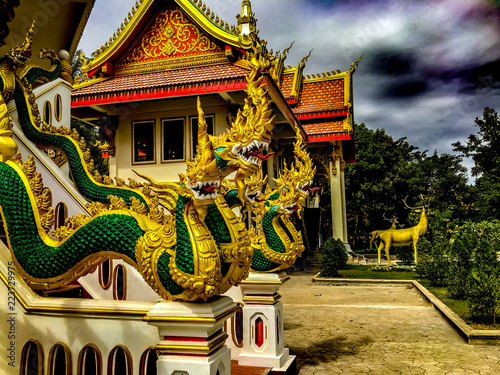 Obraz na płótnie A bright gold and green carving of the multi-headed serpant god Naga n a white staircase appearing to slither down the railing. Wat That Phoun, Vientiane Laos. w salonie