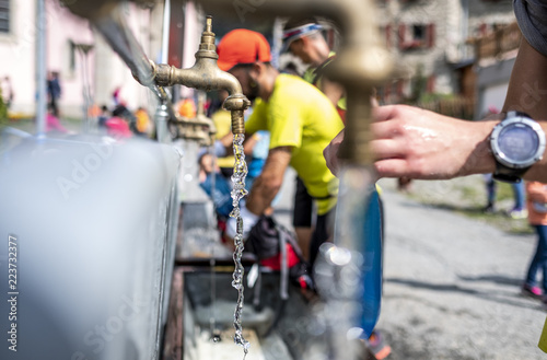 Leaking water from a tap and runners filling backpack in a mountain race © ImagineStock