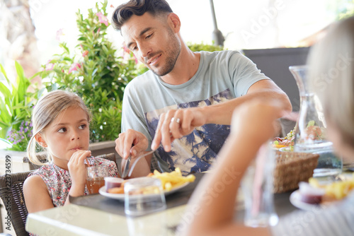 Daddy helping daughter with cutting food at restaurant