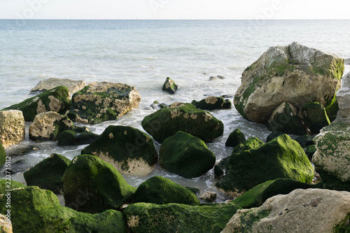 Fototapeta Małe fale uderzają w skały na plaży w słoneczny dzień.
