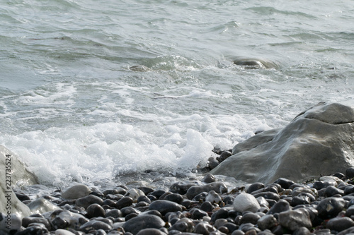 Fototapeta Małe fale uderzają w skały na plaży w słoneczny dzień.