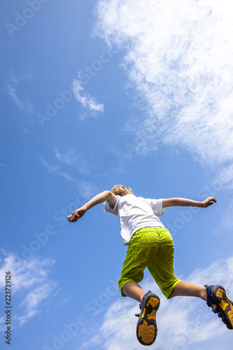 happiness, childhood, freedom, movement and people concept - happy boy jumping in air into the blue sky