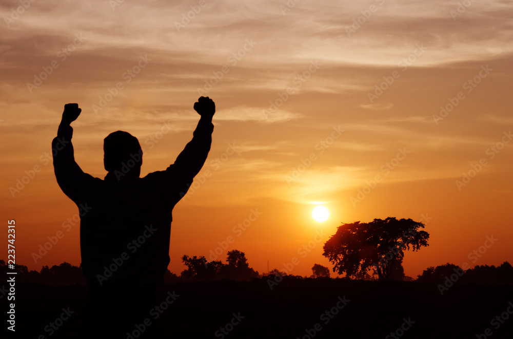 Silhouette of a man with hands raised and sunrise sky background